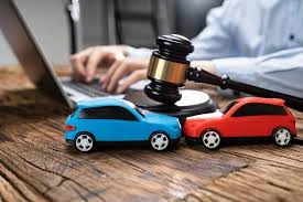 Two toy cars with a judge's gavel on top, and a car accident lawyer typing on a laptop in the background.