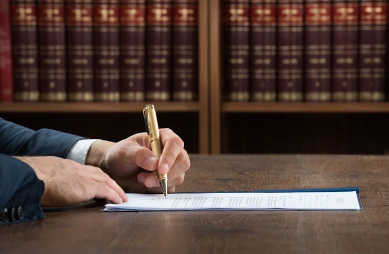 Lawyer for business formation signing a document at a wooden desk with bookshelves in the background