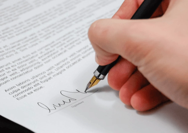 A hand holding a black pen poised to sign a document representing guest post for publication.